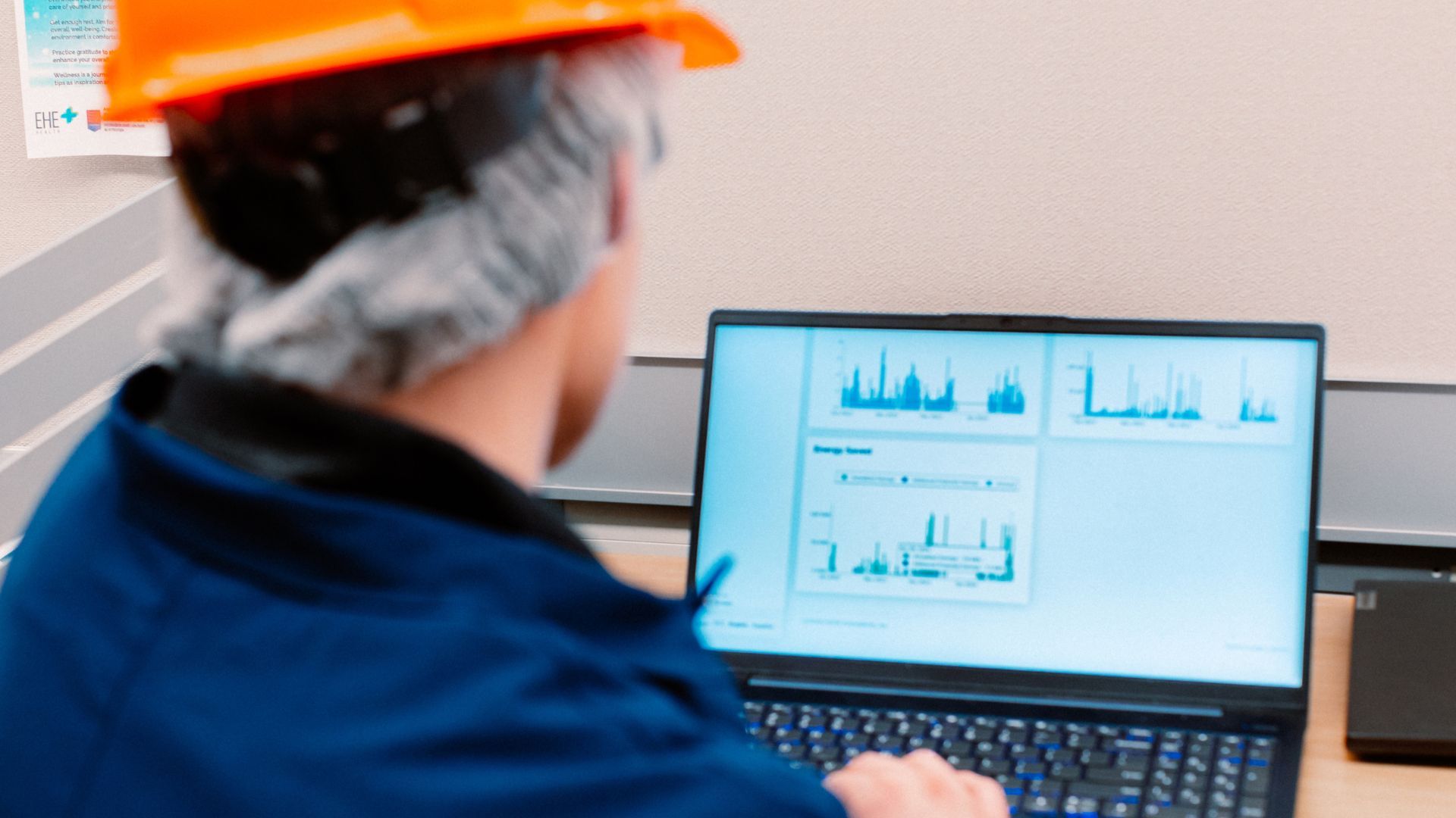 Công nhân nhà máy đội mũ bảo hộ và mặc đồng phục xanh hải quân đang đối diện với màn hình máy tính hiển thị dữ liệu và logo công ty H2Ok Innovations