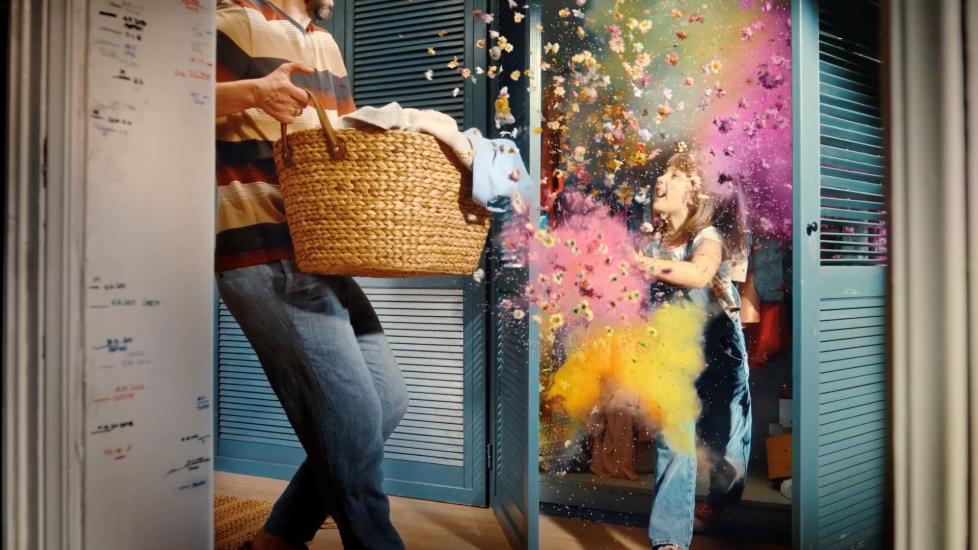 Một đứa trẻ mở tủ quần áo, bột màu sặc sỡ bắn ra trong khi người lớn đang cầm giỏ đựng quần áo.