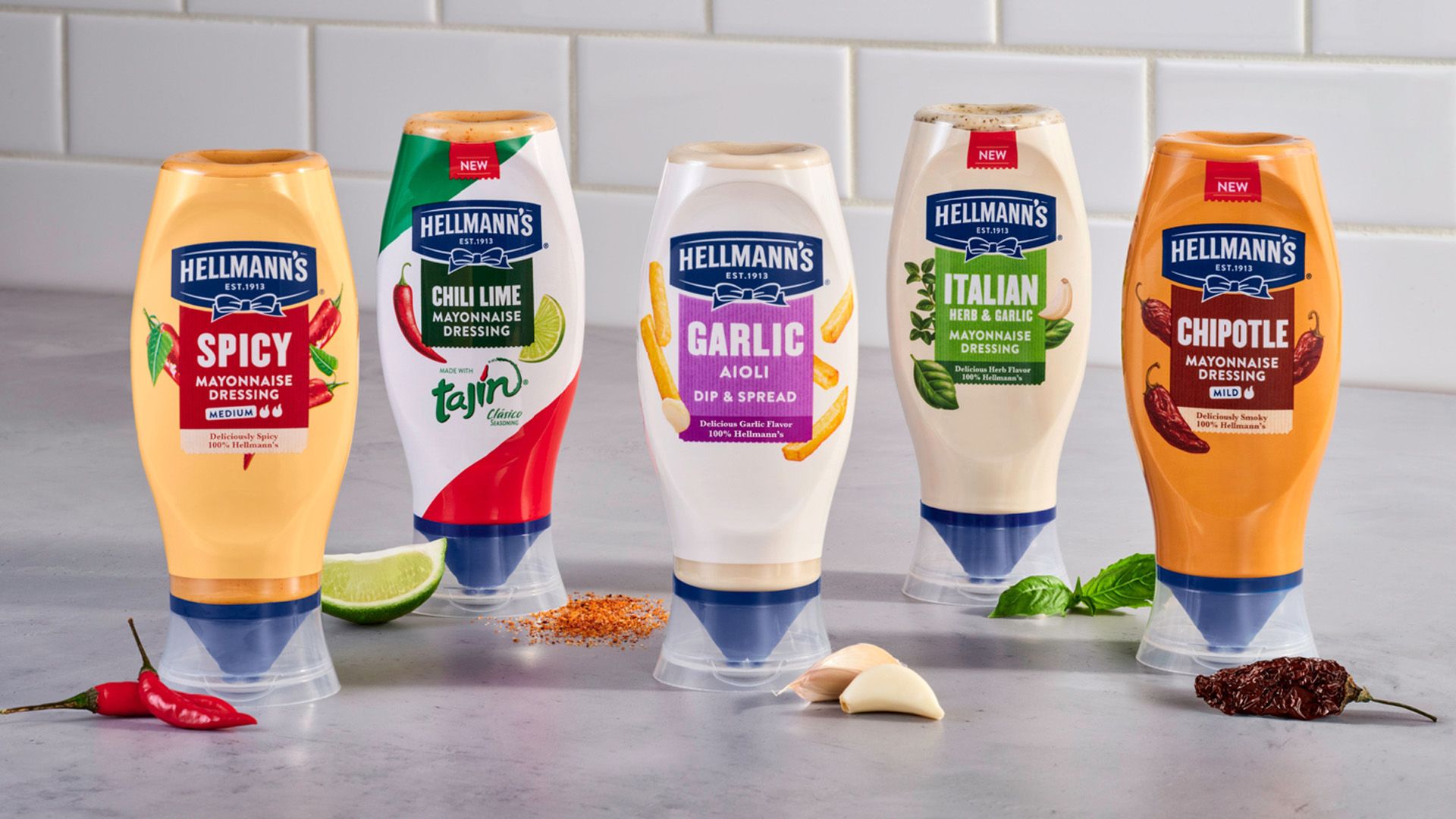 Hình ảnh các loại sốt mayonnaise nhiều hương vị đóng chai dạng bóp của Hellmann's, được trưng bày cùng các nguyên liệu chính như chanh, ớt, tỏi và các loại thảo mộc