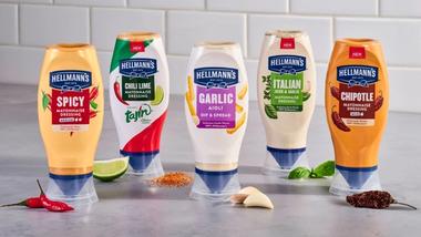 Hình ảnh các loại sốt mayonnaise nhiều hương vị đóng chai dạng bóp của Hellmann's, được trưng bày cùng các nguyên liệu chính như chanh, ớt, tỏi và các loại thảo mộc